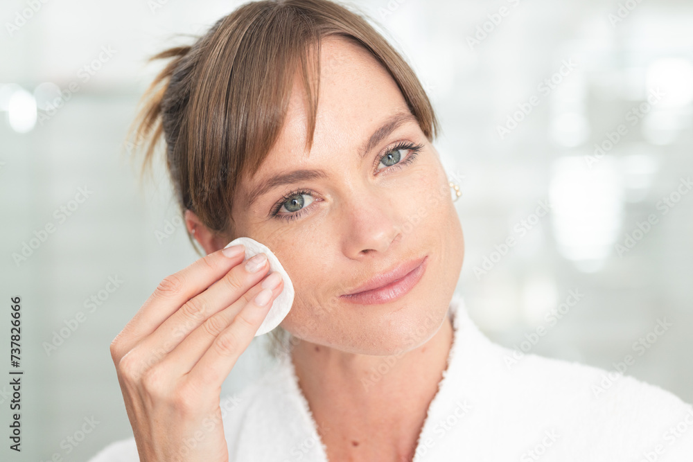 Caucasian middle-aged woman applies skincare in a bright bathroom Caucasian middle-aged woman applies skincare in a bright bathroom