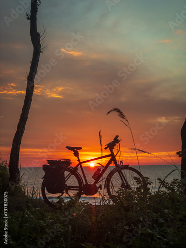 A serene sunset scene with a bicycle silhouette against a vibrant orange sky by the tranquil sea.