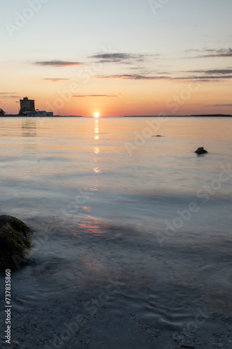 Tramonto sul mare con l'acqua ad effetto seta e torre costiera sullo sfondo. photo