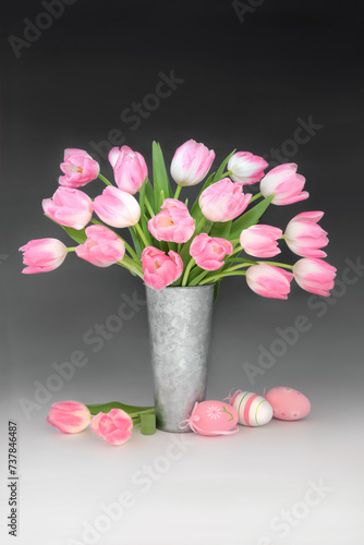 Fototapeta Naklejka Na Ścianę i Meble -  Pink Easter eggs and tulip flower still life arrangement in metal vase on gradient black white background. Spring and Easter floral nature design.