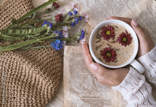 Female hands holding a cup of cappuccino with flowers on a book background