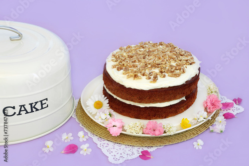 Carrot and walnut cake for birthday party with summer flowers and cake tin cover on purple background. Homemade delicious food concept.