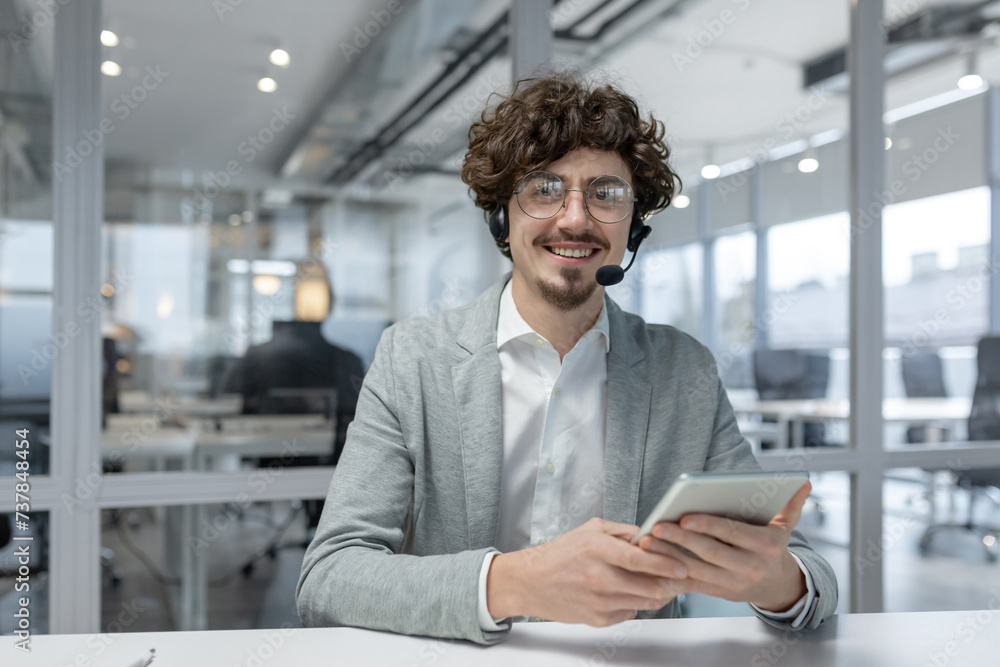 Charismatic young professional with curly hair and headset confidently working in a contemporary office environment, using a tablet. Charismatic young professional with curly hair and headset confidently working in a contemporary office environment, using a tablet.