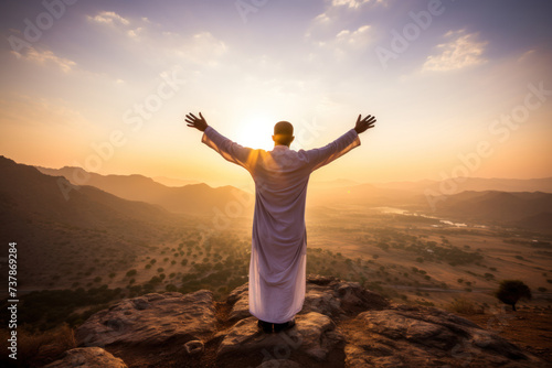 Man in white robe celebrates Ramadan on mountain at sunset
