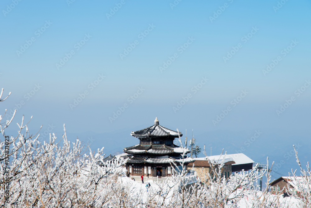 a traditional Korean building on the top of the snow-covered mountain
