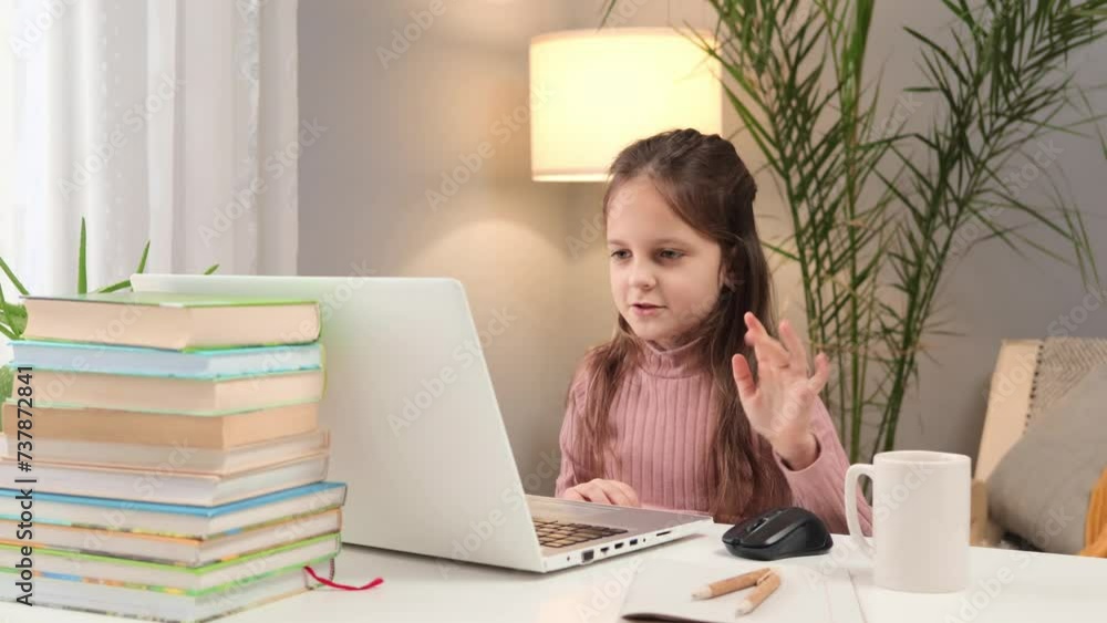 Child attending online school. Distance learning with a laptop. Caucasian little brown haired girl using laptop studying online at home waving hand showing hello gesture during video call Child attending online school. Distance learning with a laptop. Caucasian little brown haired girl using laptop studying online at home waving hand showing hello gesture during video call