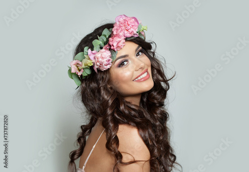 Pretty woman with make-up, perfect white toothy smile and spring or summer season rose flower wreath on her long healthy shiny wavy hair, fashion beauty studio portrait