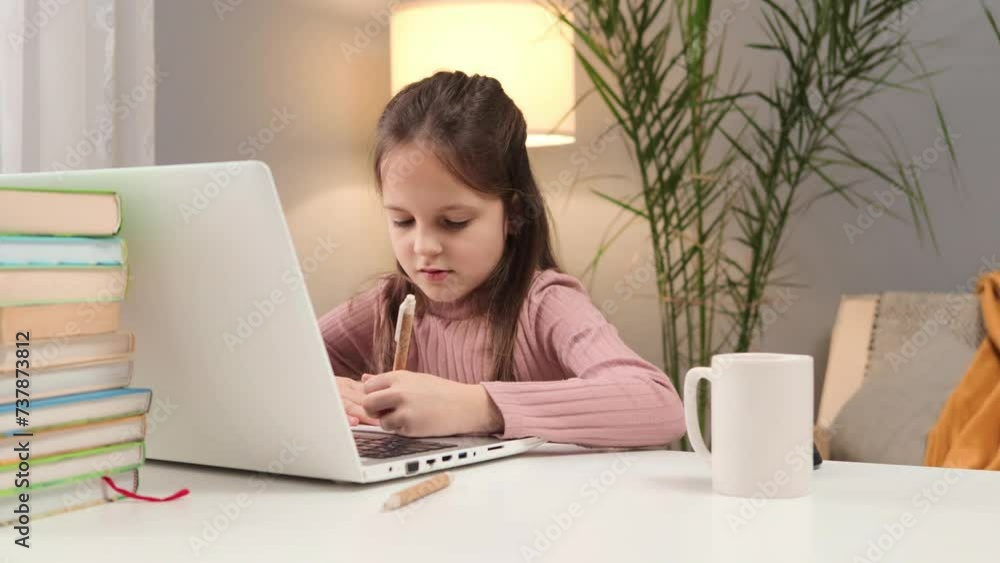 Online lesson for a schoolgirl. Studying at home with a notebook. Child participating in a video call. Caucasian little brown haired girl using laptop studying online at home writing down information Online lesson for a schoolgirl. Studying at home with a notebook. Child participating in a video call. Caucasian little brown haired girl using laptop studying online at home writing down information
