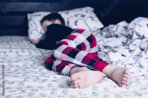 Bare feet of a child. A child in pajamas. Bare feet sticking out from under the blankets. The boy is sleeping in bed. Foot and leg