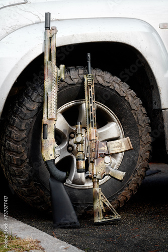A shotgun and a rifle gun standing against the wheel of a silver SUV photo