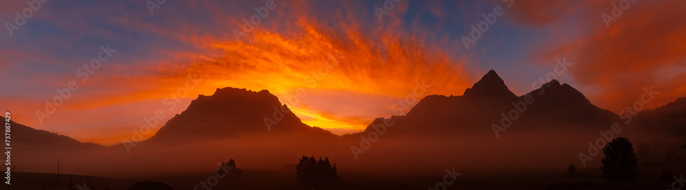 High resolution stitched alpine summer sunrise panorama with a foggy view of Mount Zugspitze at Lermoos, Reutte, Tyrol, Austria