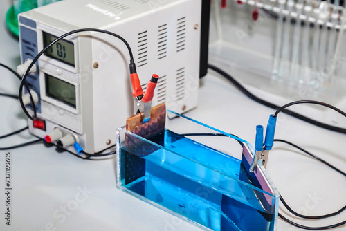Equipment for electrolysis and container with blue acid in chemical laboratory, electroanalysis process. Reagents suspensions for experiment on lab table. Chemical industry concept. Copy ad text space photo