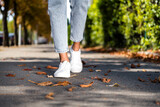 Cropped photo of female legs in white trendy sneakers going on shopping asphalt pavement