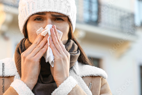 Woman with tissue blowing runny nose outdoors. Cold symptom