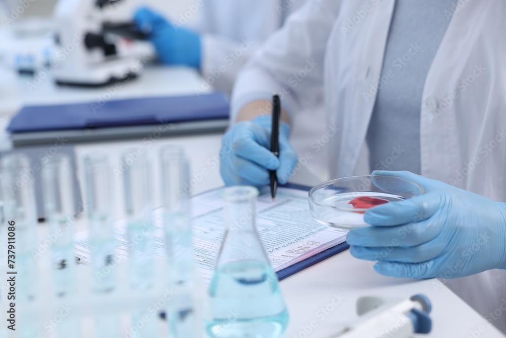 Laboratory worker holding petri dish with blood sample while working at white table, closeup