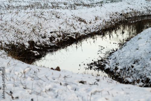 The bending Molenbeek creek through the snowy meadows in Jette, Belgium