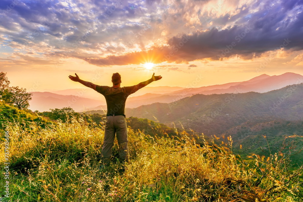 rejoicing man with beautiful scenic mountain sunset landscape on background. happy man watching amazing evening sunset