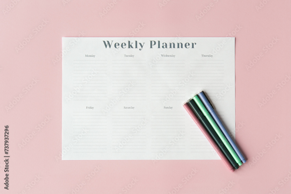 white weekly planner sheet on pink background and four colored pens, planning concept white weekly planner sheet on pink background and four colored pens, planning concept
