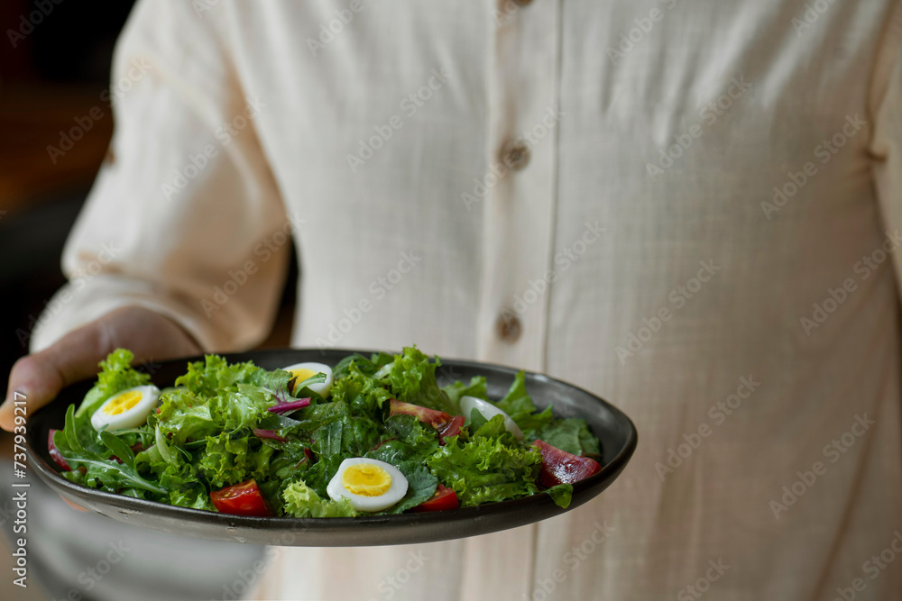 Close-up of a man holding a bowl of salad with eggs and cherry tomatoes. Waiter