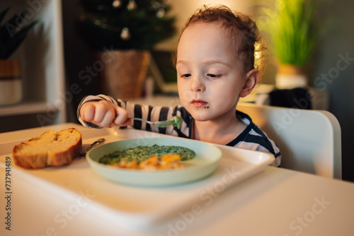 A little boy is eating his lunch on his own at home.