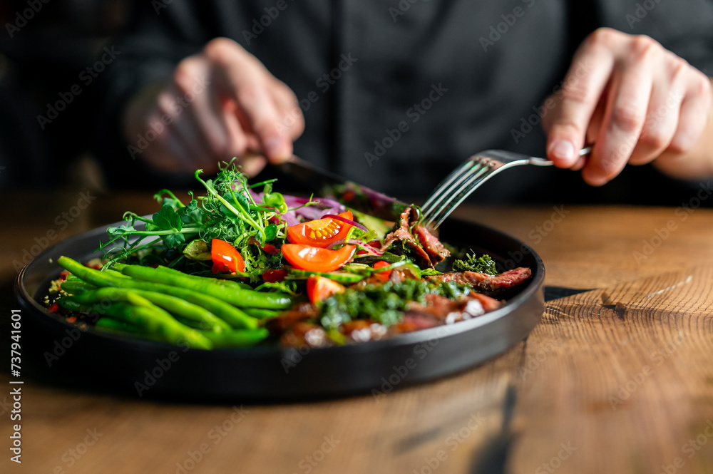Hands of a man with a fork and knife eat Salad