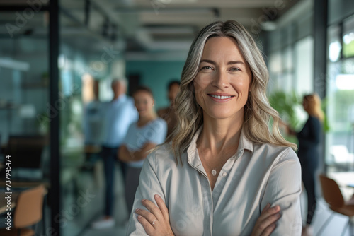 Smiling successful Businesswoman with crossed arms and diverse team in background in office setting