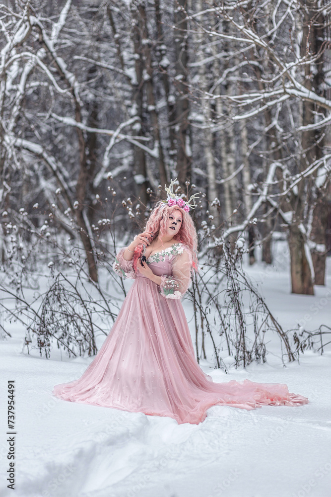 A beautiful spring fairy, a dryad with deer antlers and a crown and a light pink dress in a snowy forest.A fabulous photo. The concept of changing seasons. A beautiful spring fairy, a dryad with deer antlers and a crown and a light pink dress in a snowy forest.A fabulous photo. The concept of changing seasons.