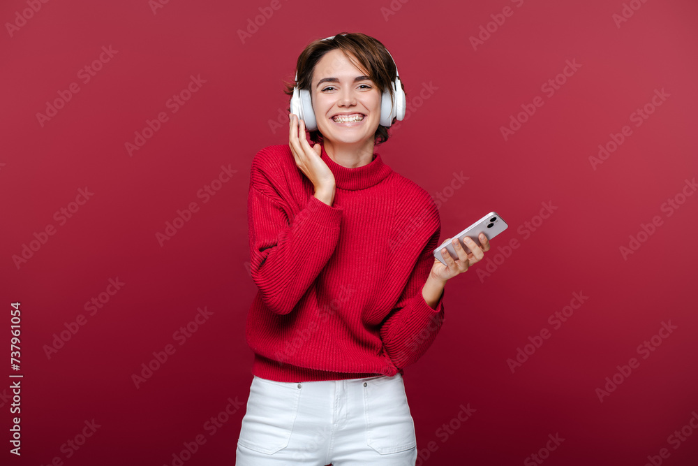 Naklejka premium Smiling happy young woman wearing red turtleneck, listening to music in headphones