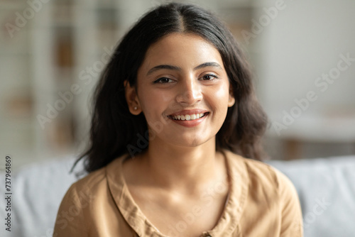 Portrait of young indian woman resting at home, joyful lady sitting on comfortable sofa and smiling at camera, enjoying domestic pastime © Home-stock
