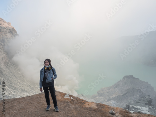 The girl is standing in front of lake full of natural Sulfuric acid and hydrogen sulfide gas inside the volcano carter at Kawah Ijen, East Java, Indonesia.