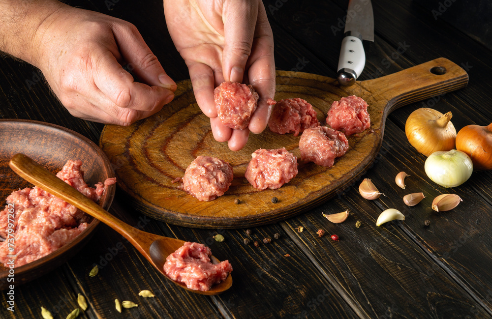 The chef hand holds a ground beef meatball ready for cooking. The concept of cooking cutlets on the kitchen table with aromatic spices