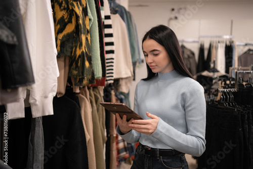 Business woman inspecting garment in her clothes shop. Beautiful shop owner conducting a control check in her clothing boutique using digital tablet.