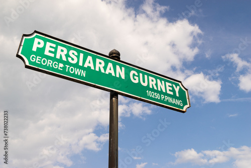 Gurney Drive street sign in George Town, Penang, Malaysia with blue sky and white clouds as background.