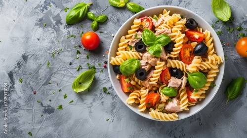 Fusilli pasta salad with tuna, tomatoes, black olives and basil on gray stone background. Top view. photo