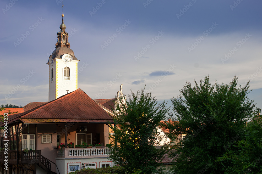 Obraz premium church bell tower with a clock in the background of a rural house in an alpine Slovenian village