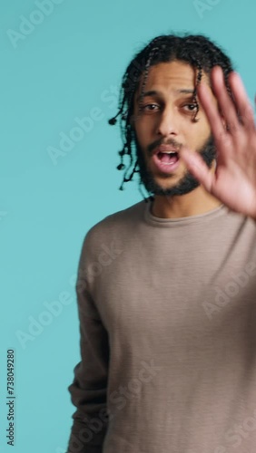 Vertical video Assertive african american man doing stop hand gestures. Annoyed BIPOC person doing firm halt sign gesturing, wishing to end concept, isolated over blue studio background, camera A photo