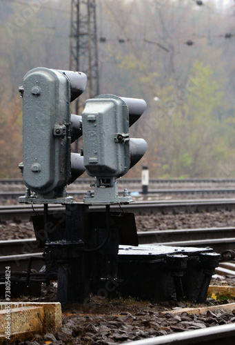 Photo of a fragment of a railway track with a small traffic light in rainy weather