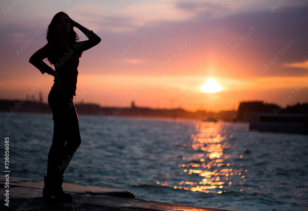 a silhouette of a woman standing in front of a body of water at sunset
