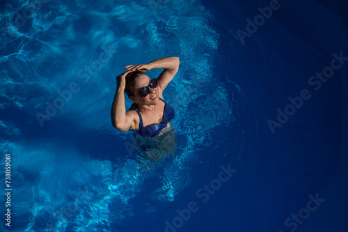 An elderly woman in sunglasses swims in the pool. Vacation in retirement. 