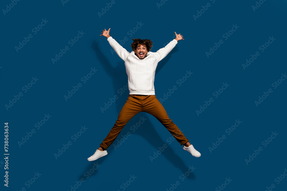 Full length photo of excited funky guy dressed white pullover jumping high like star isolated dark blue color background