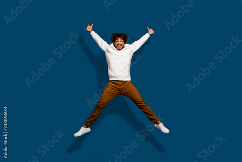Full length photo of excited funky guy dressed white pullover jumping high like star isolated dark blue color background