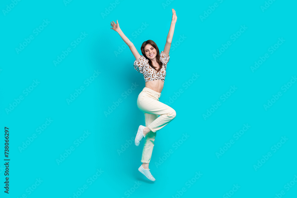 Full length photo of funky excited lady dressed flower print top rising hands arms jumping high isolated turquoise color background