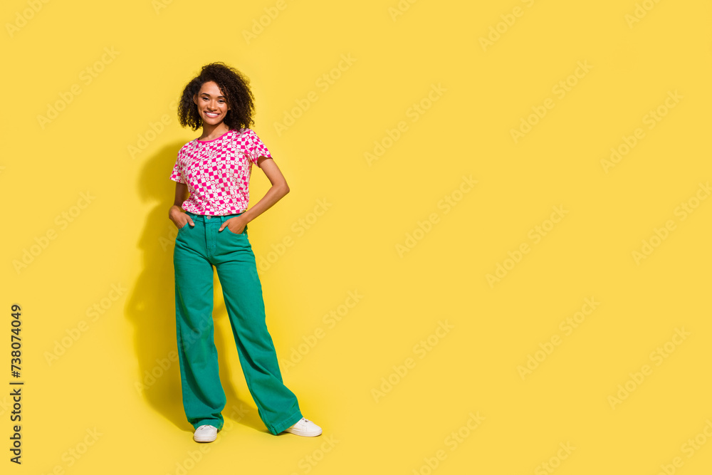 Full size photo of nice cheerful girl put hands pockets posing empty space ad isolated on yellow color background Full size photo of nice cheerful girl put hands pockets posing empty space ad isolated on yellow color background