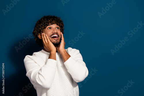 Photo of young funny crazy guy in white jumper touch cheeks looking empty space staring impressed isolated on dark blue color background