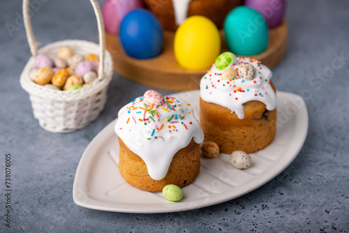 Two small Easter kulichs with candied fruits in white glaze with colorful sprinkles in the cut. Painted chicken and quail eggs. Traditional Easter baking. Easter holiday. Close-up, selective focus. photo