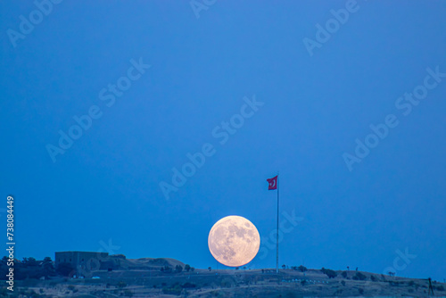 This captivating image captures the full moon rising majestically behind a Turkish flag atop an ancient bastion in Erzurum, Turkey.12 March Liberation of Erzurum from Enemy Occupation. photo