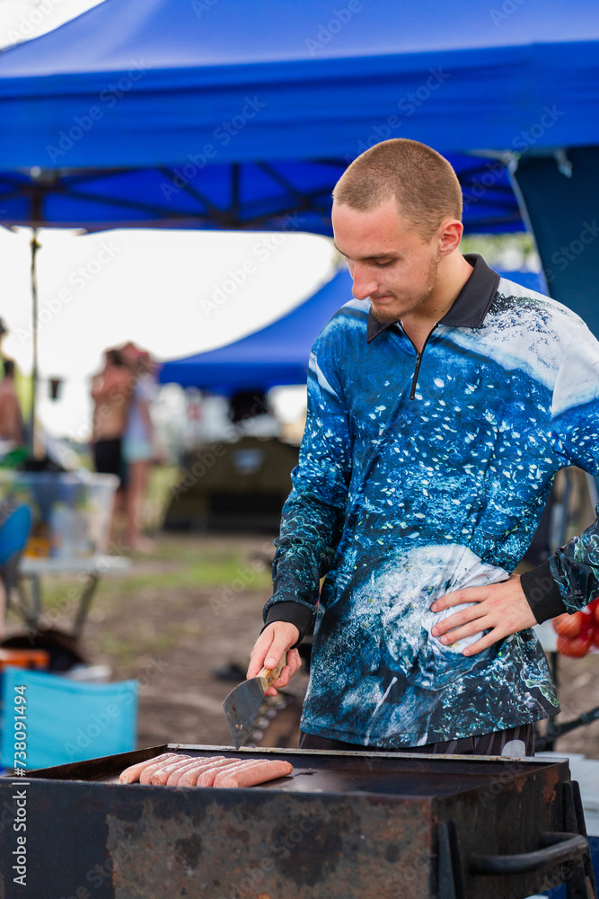 Young Australian person cooking sausages he made on BBQ at campground Young Australian person cooking sausages he made on BBQ at campground