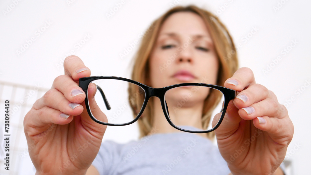 Close-up of black-framed glasses in the hands of a young woman