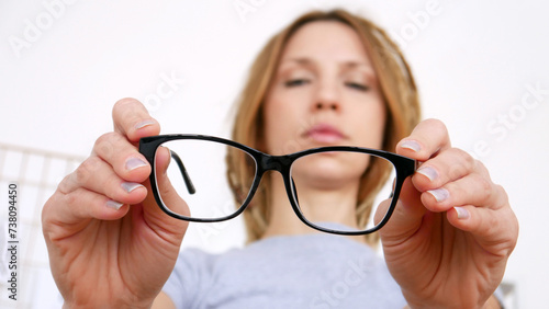 Close-up of black-framed glasses in the hands of a young woman