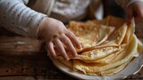 Child's hand reaching for a stack of homemade pancakes on a wooden table. Golden crepes with sugar sprinkled by a child for a sweet breakfast.